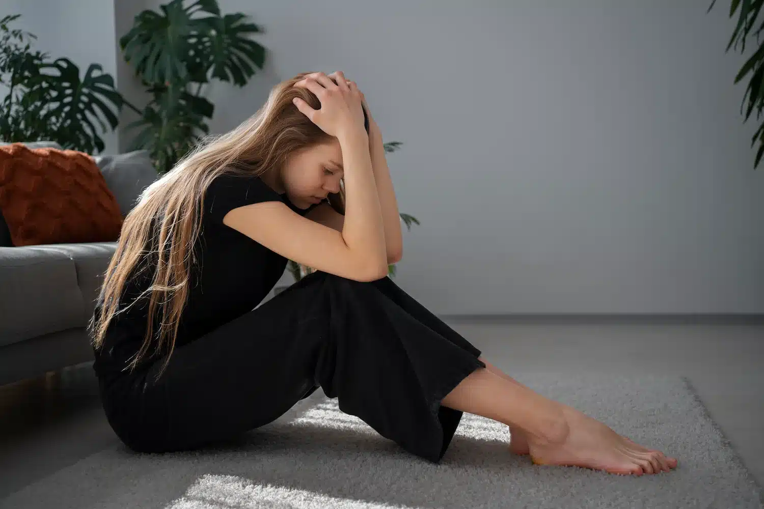 jeune femme assise au sol, la tête dans les mains, exprimant une détresse émotionnelle dans un intérieur lumineux